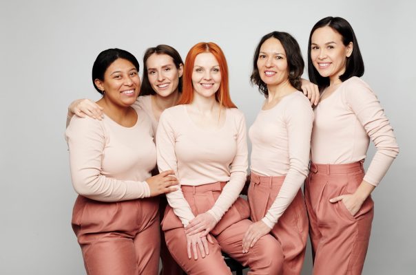 Portrait of smiling interracial women in same pink outfits standing together against isolated background
